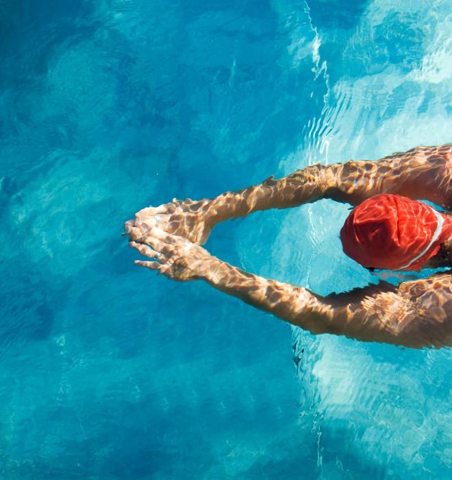 Nuotatore in piscina con cuffia rossa e costume blu.