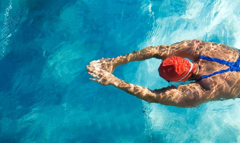 Nuotatore in piscina con cuffia rossa e costume blu.