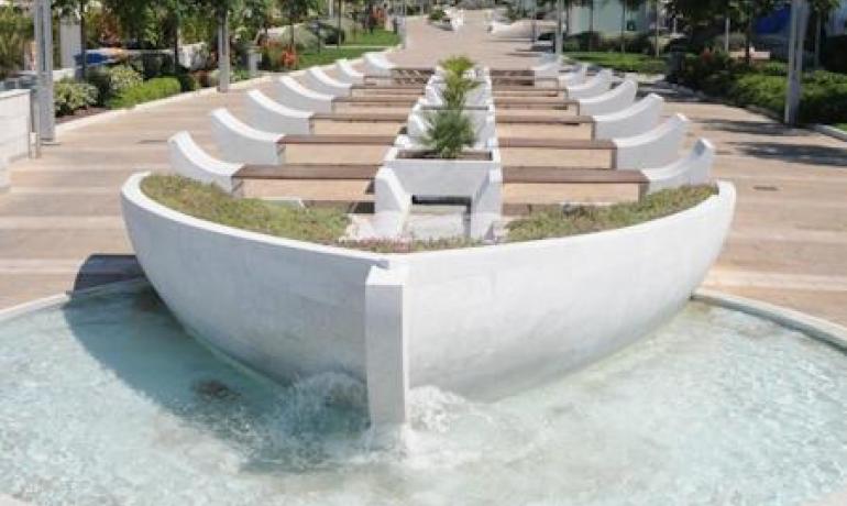 Fontana moderna con piante e acqua in un viale alberato.