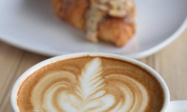 Cappuccino con latte art e croissant su piatto bianco.