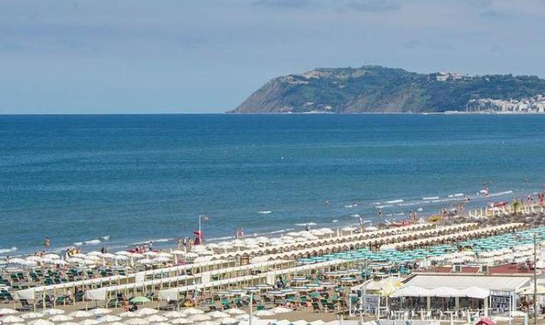 Spiaggia affollata con ombrelloni e mare blu, vista panoramica.