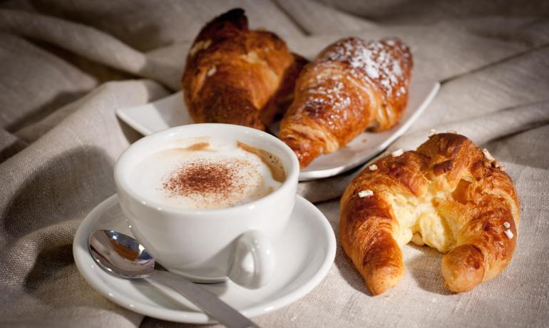 Colazione con cappuccino e croissant su tovaglia.