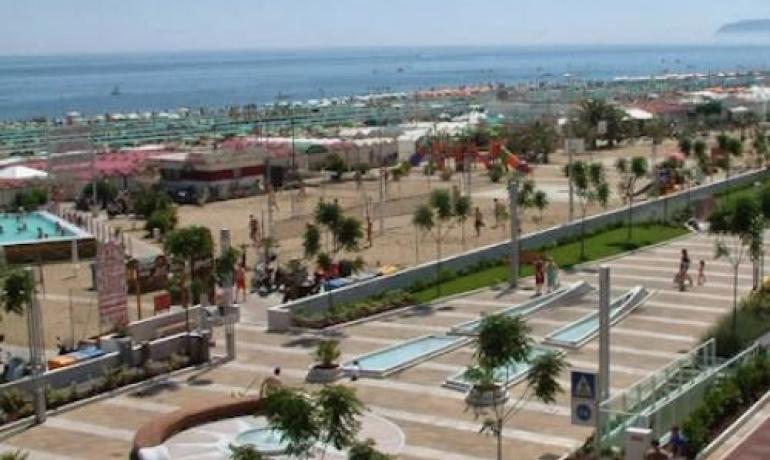 Spiaggia affollata con pista ciclabile e mare azzurro.