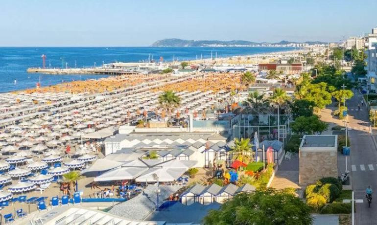 Spiaggia affollata con ombrelloni colorati e mare blu.