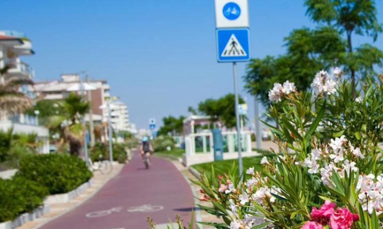 Pista ciclabile con fiori e segnale stradale sotto un cielo azzurro.