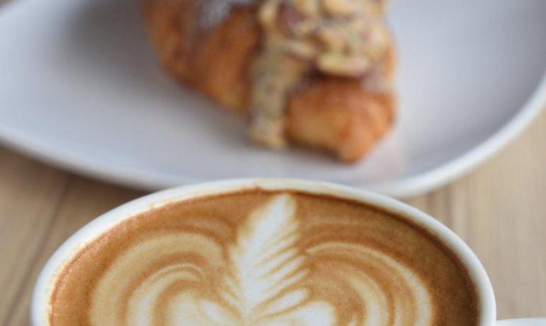 Cappuccino con latte art e croissant su un piatto.