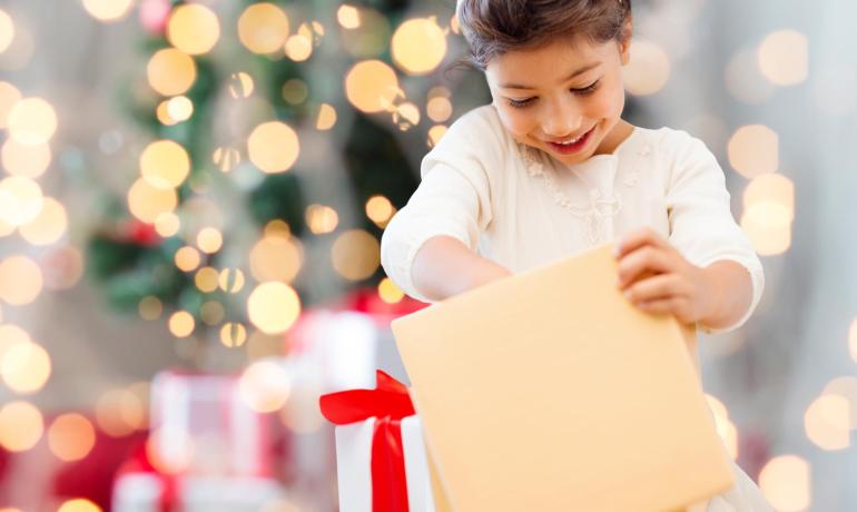 Bambina felice apre regalo di Natale con luci sullo sfondo.