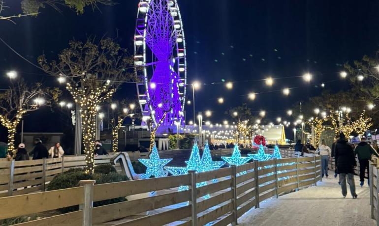 Pista di pattinaggio con luci natalizie e ruota panoramica.