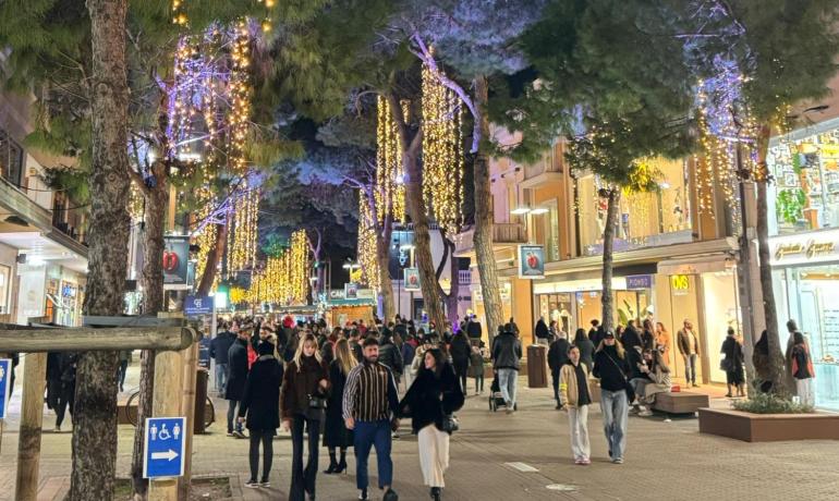 Strada pedonale illuminata con luci natalizie e persone passeggiando di sera.