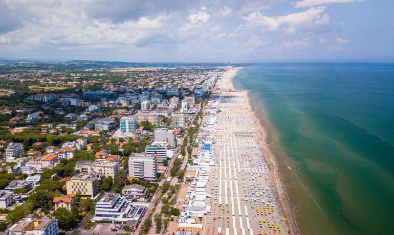 Vista aerea di una lunga spiaggia con ombrelloni e città vicina.