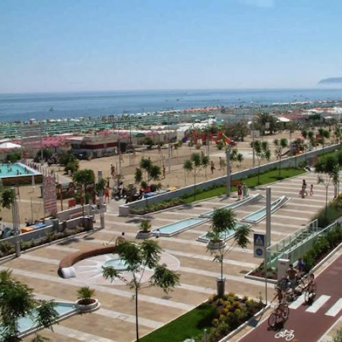 Spiaggia affollata con pista ciclabile e mare azzurro, perfetta per una giornata estiva.